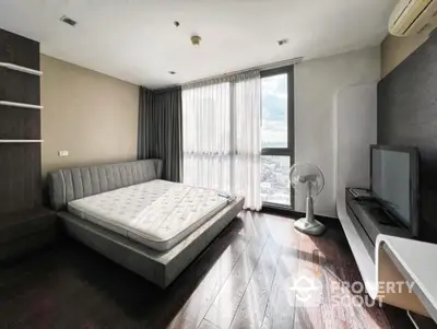 Modern bedroom with large window and city view, featuring sleek furniture and wooden flooring.