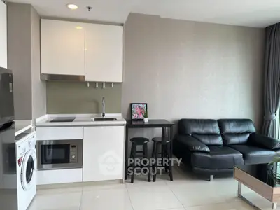 Modern living room with sleek kitchen, black leather sofa, and washing machine in a stylish apartment.
