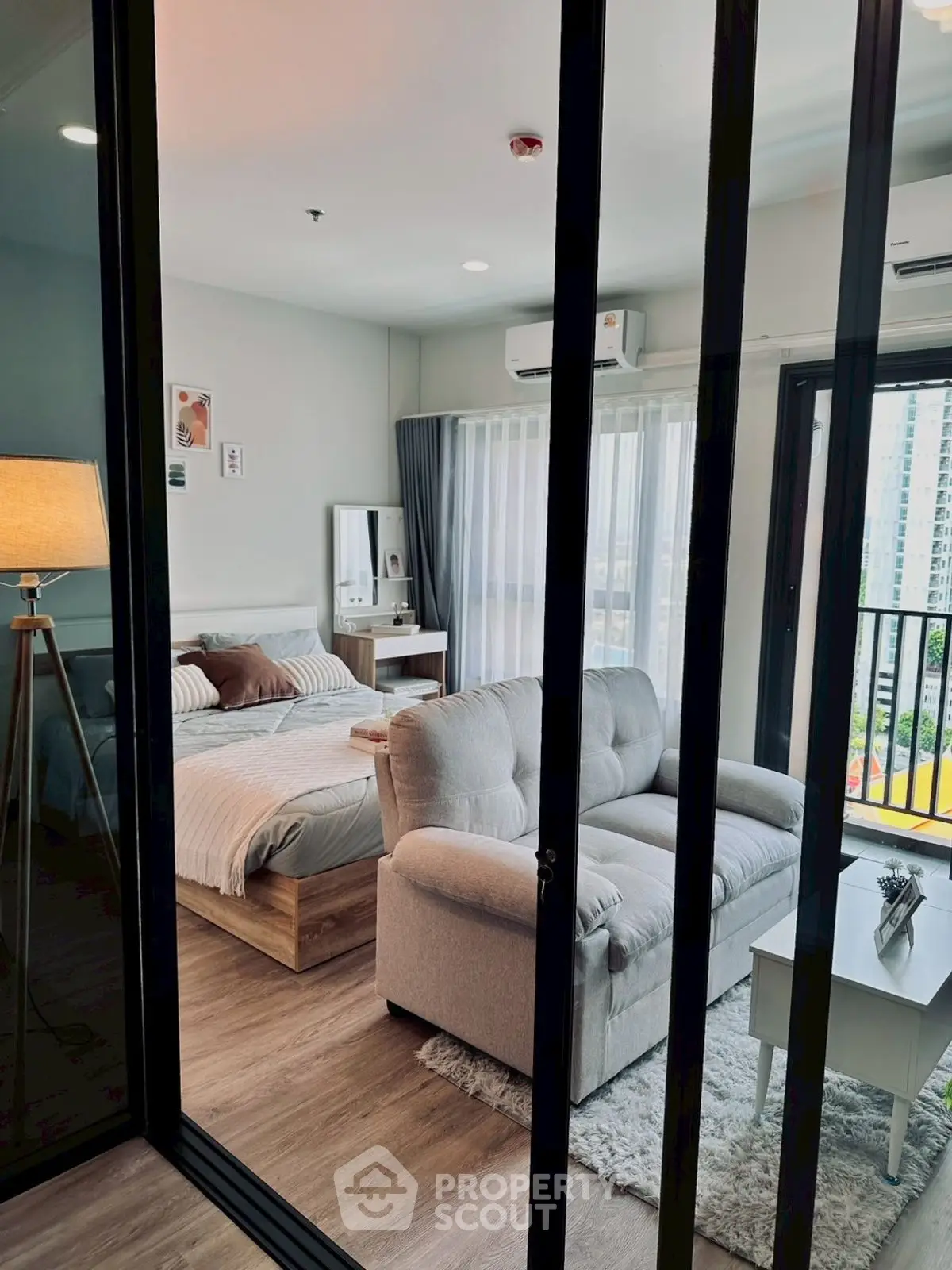 Modern studio apartment with cozy living area and bedroom, featuring a large window and stylish decor.