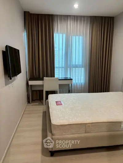 Cozy bedroom with modern decor and natural light, featuring a comfortable bed and wall-mounted TV.