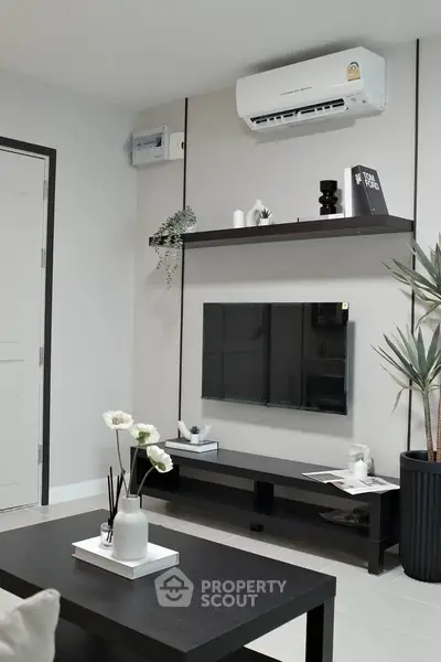 Modern living room with sleek black furniture and wall-mounted TV, featuring minimalist decor and air conditioning.