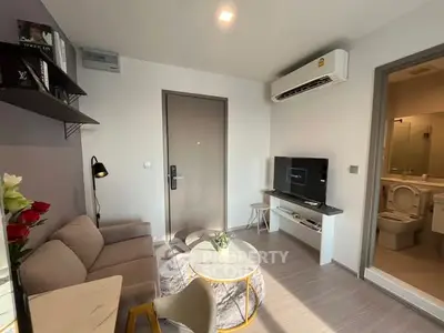 Modern living room with cozy sofa, wall-mounted TV, and air conditioning, adjacent to a bathroom.