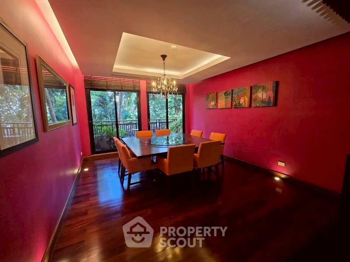 Elegant dining room with vibrant pink walls and large windows overlooking lush greenery.