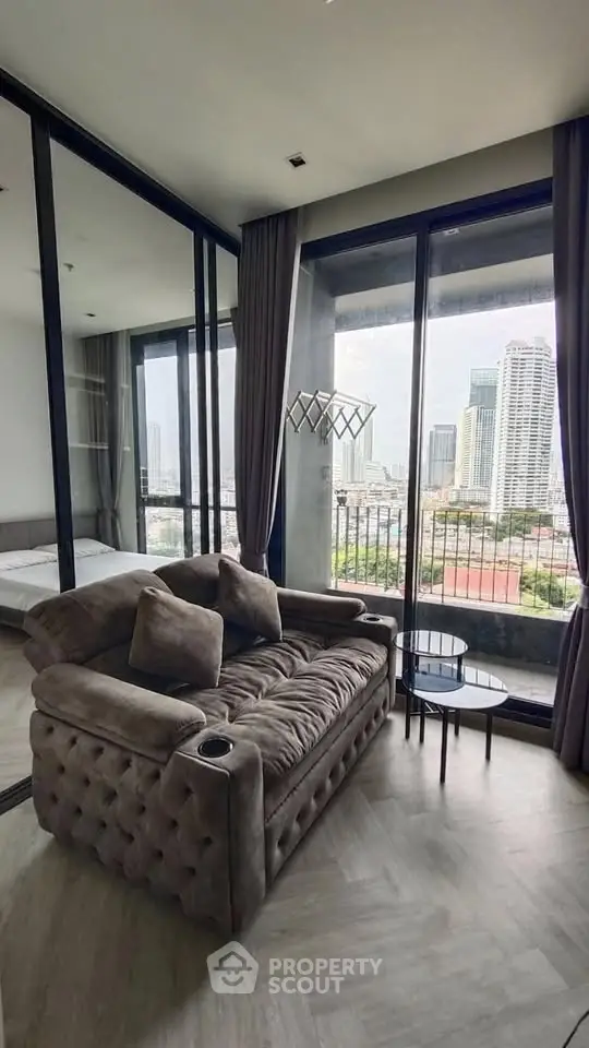 Modern living room with plush sofa and city view from large windows in high-rise apartment.