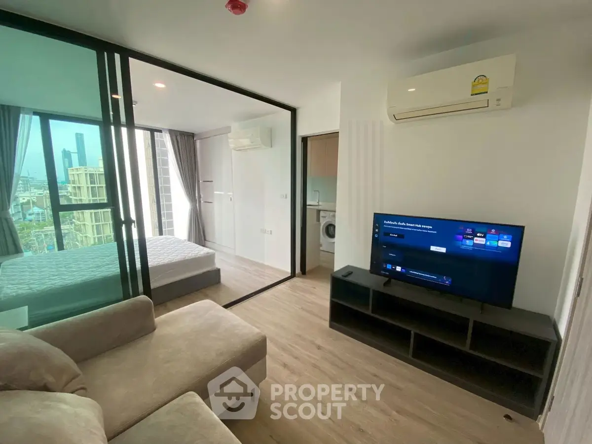 Modern condo living room with TV, sofa, and view into bedroom, featuring sleek design and natural light.