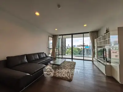 Spacious living room with modern decor and city view, featuring large windows and sleek furniture.