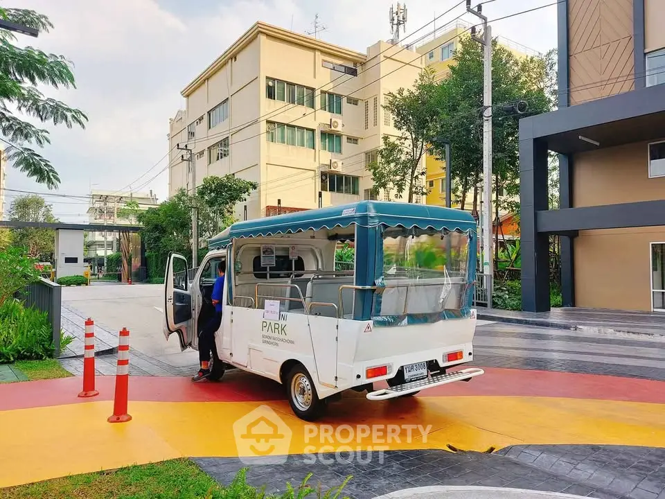 Modern residential complex entrance with shuttle service in vibrant urban setting.