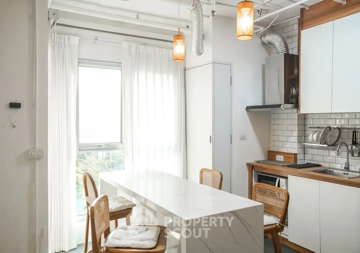 Modern kitchen with sleek white cabinetry and dining area, featuring natural light and stylish lighting fixtures.