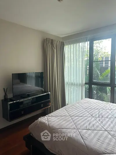 Cozy bedroom with large window and modern TV setup, perfect for relaxation.