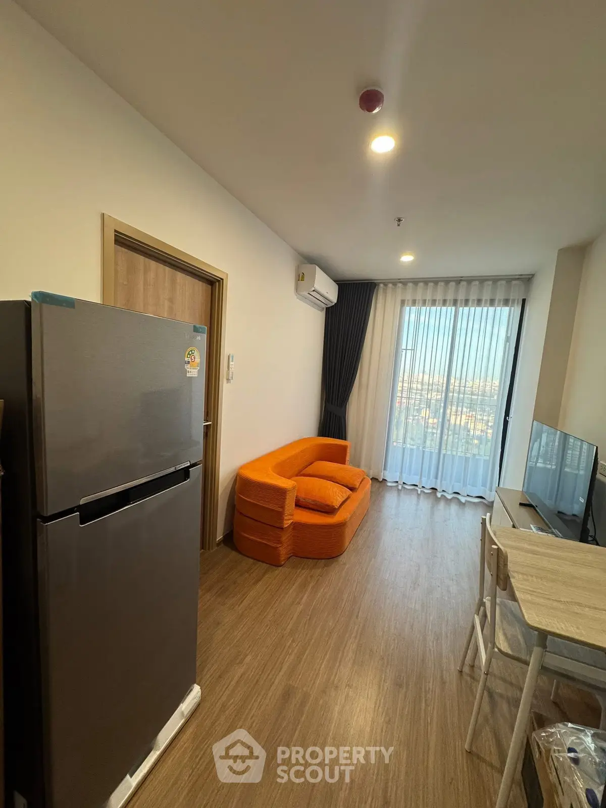 Modern living room with orange sofa, large window, and sleek appliances in a cozy apartment.