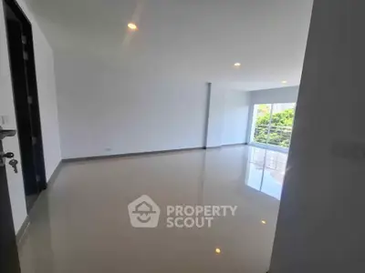 Spacious empty living room with glossy floors and large windows offering natural light and greenery view.