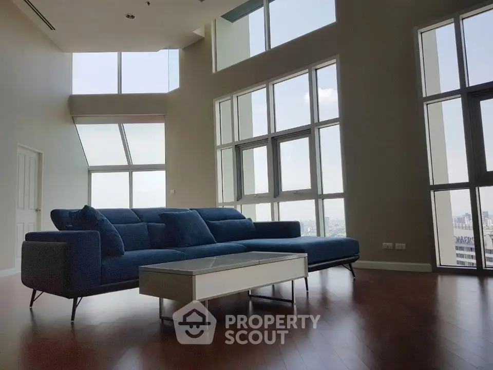 Spacious modern living room with large windows and city view, featuring a stylish blue sofa and sleek coffee table.