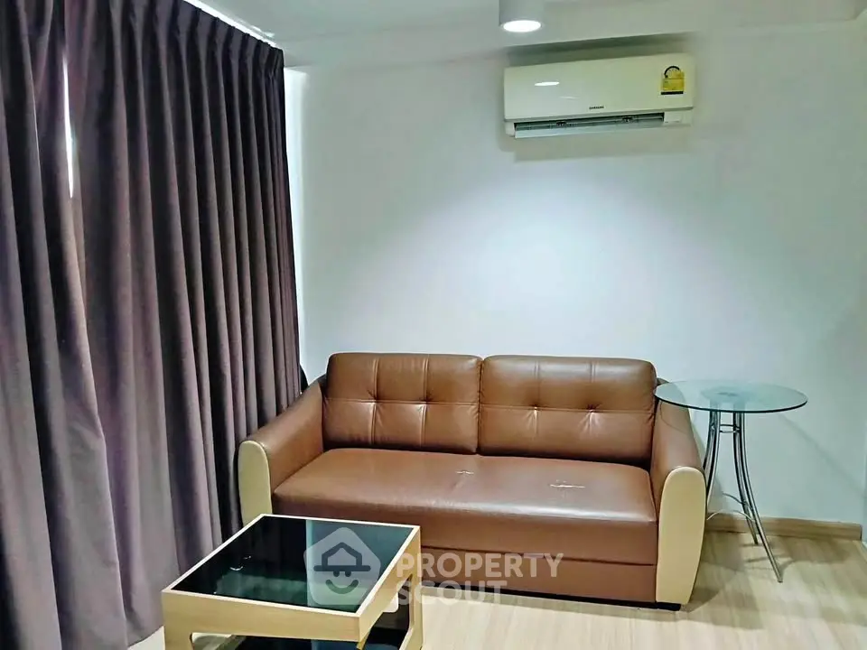 Cozy living room with brown leather sofa, glass coffee table, and air conditioning.