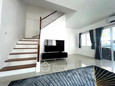 Modern living room with sleek staircase and large TV, featuring elegant decor and natural light.