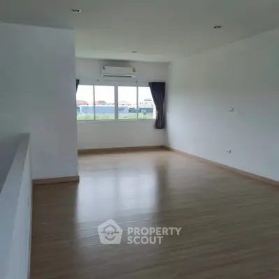Spacious empty room with wooden flooring and large window offering natural light and city view.