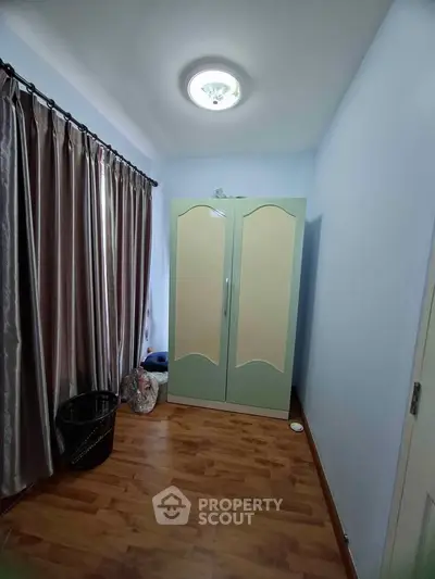 Cozy small bedroom with wooden flooring and elegant curtains, featuring a stylish wardrobe.