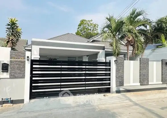 Modern single-story house with sleek black gate and tropical landscaping.