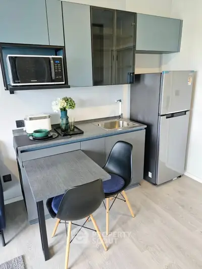 Modern compact kitchen with sleek cabinetry, dining area, and stainless steel appliances in a stylish apartment.