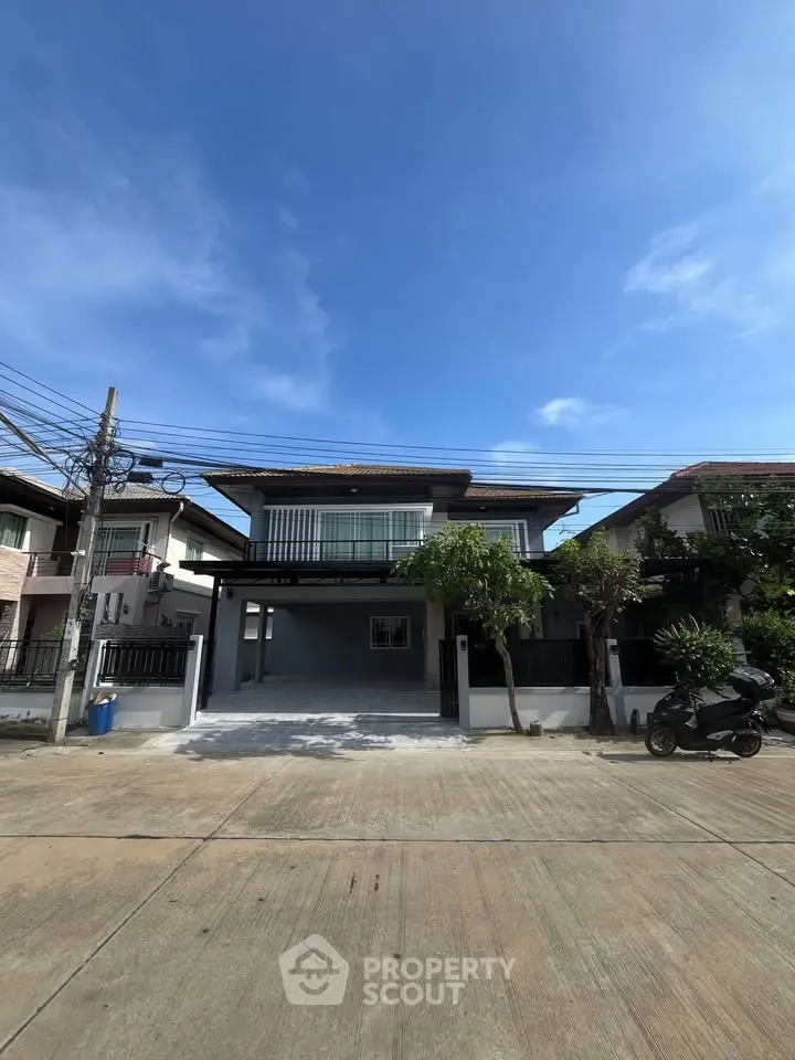 Modern two-story house with spacious driveway and lush greenery under clear blue sky.