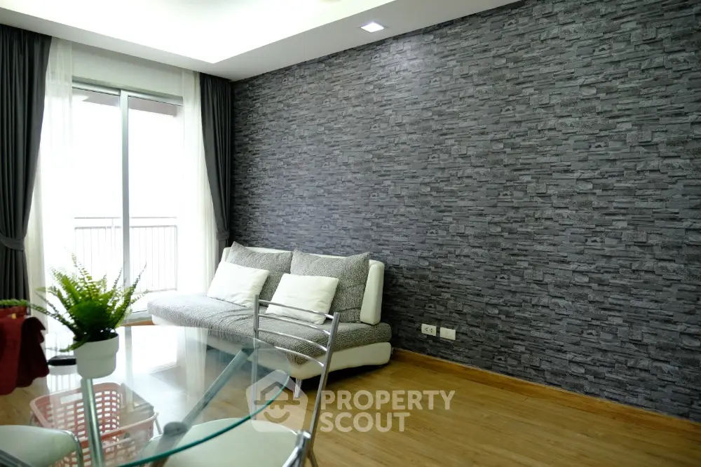 Modern living room with stone accent wall and glass table, featuring cozy sofa and natural light.