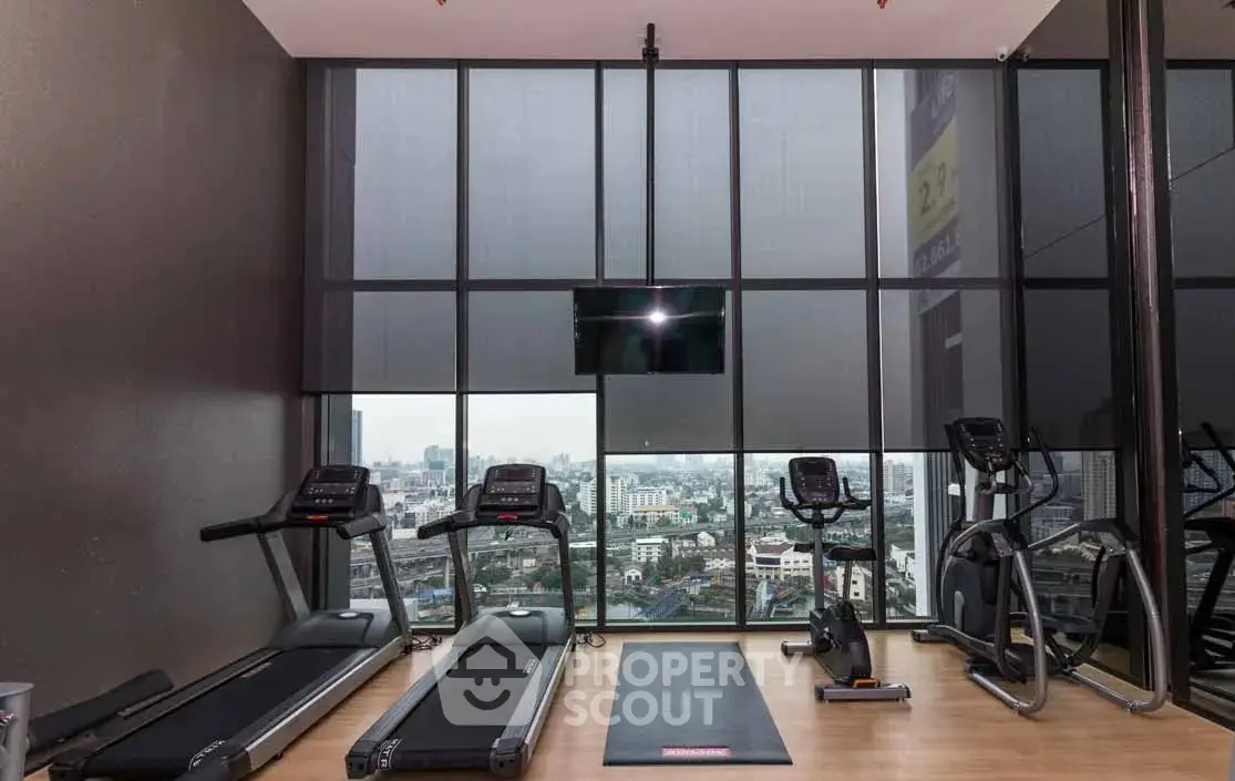 Modern gym with city view, featuring treadmills and exercise equipment in a high-rise building.