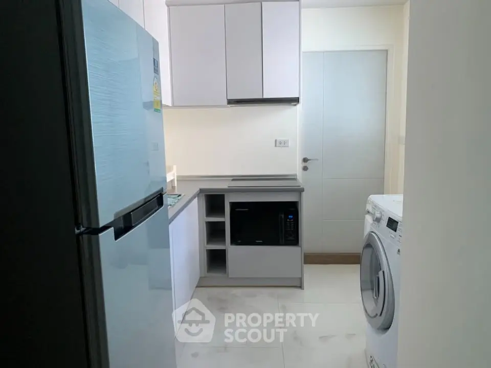 Modern kitchen with sleek appliances including fridge, microwave, and washing machine in a compact layout.