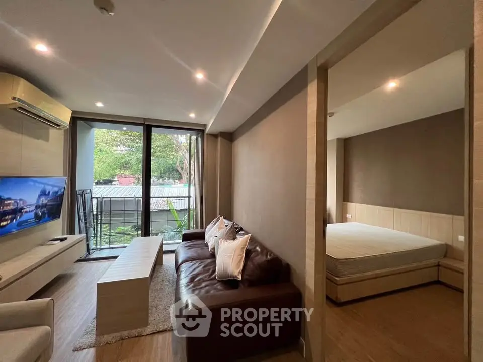 Modern living room with cozy seating and adjacent bedroom, featuring large windows and stylish decor.