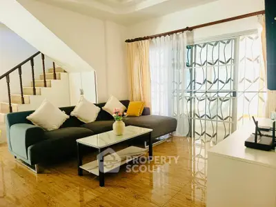 Spacious living room with modern sofa and elegant decor, featuring a staircase and large windows for natural light.
