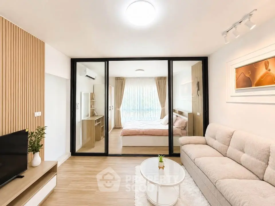Modern living room with glass partition leading to a cozy bedroom, featuring elegant decor and natural light.