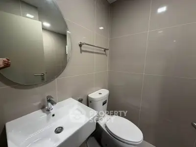 Modern bathroom with sleek fixtures and neutral tiles, featuring a round mirror and compact design.