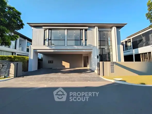 Modern two-story house with large windows and spacious driveway in a sunny neighborhood.