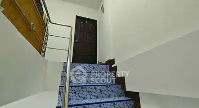 Stylish staircase with blue mosaic tiles leading to a wooden door in a modern home.