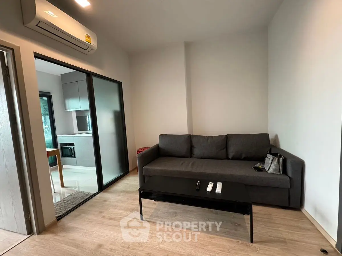 Modern living room with sleek gray sofa and air conditioning, adjacent to a stylish kitchen.