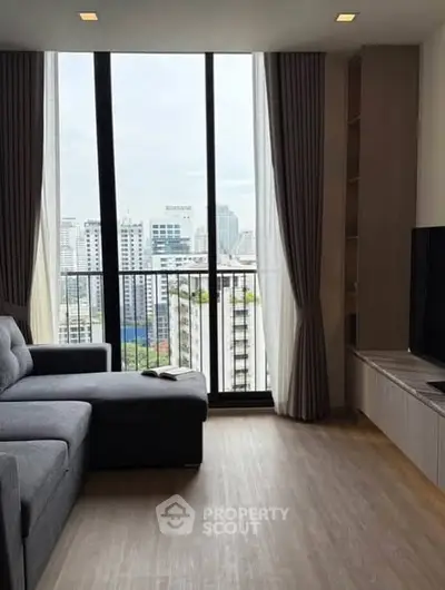 Modern living room with large windows offering stunning city views, featuring a comfortable gray sofa and sleek entertainment unit.