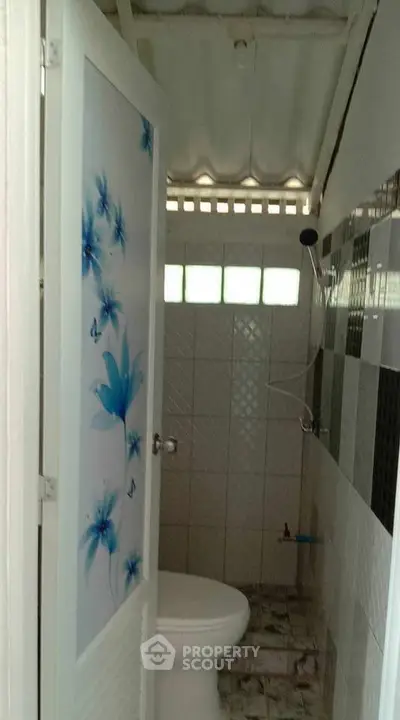 Compact bathroom with floral door design and tiled interior.