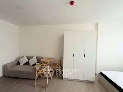 Modern minimalist bedroom with cozy sofa, wooden dining set, and sleek wardrobe.