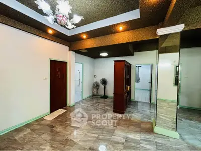 Spacious living room with elegant chandelier and mirrored wall, featuring modern flooring and ample natural light.