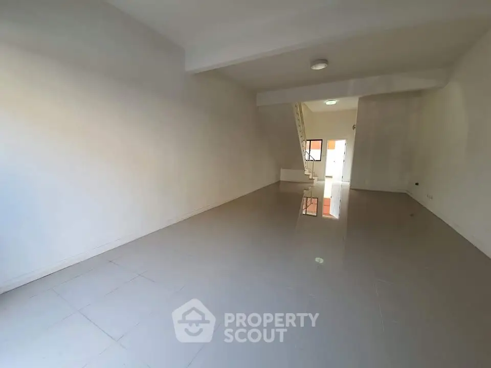 Spacious empty room with glossy tiled floor and staircase, ideal for customization.