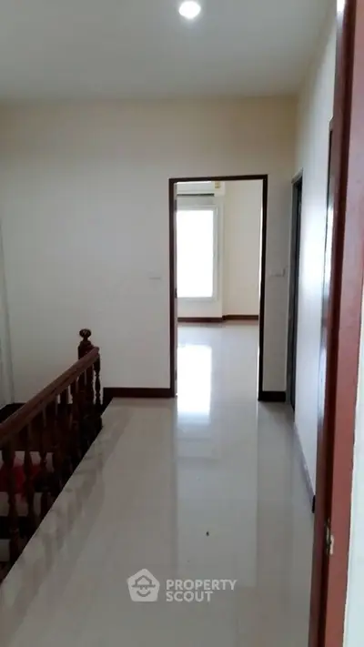 Bright hallway with polished floors and wooden railing leading to a sunlit room.