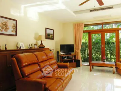 Spacious living room with leather sofas and garden view, featuring elegant decor and natural light.