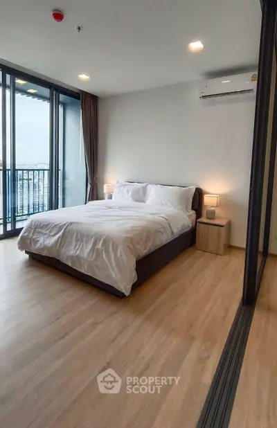 Spacious modern bedroom with large windows and city view, featuring sleek wooden flooring and contemporary furnishings.