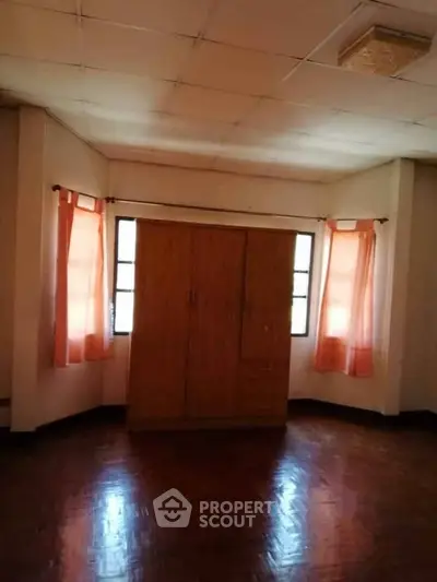 Spacious bedroom with wooden wardrobe and natural light from windows.