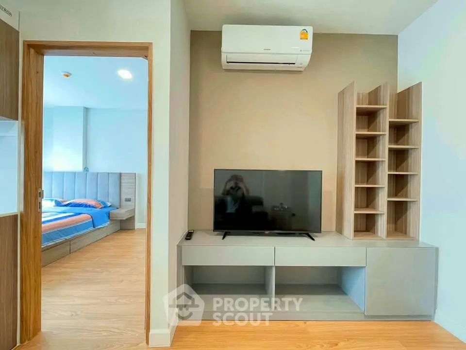 Modern living room with TV, air conditioning, and view into a stylish bedroom.