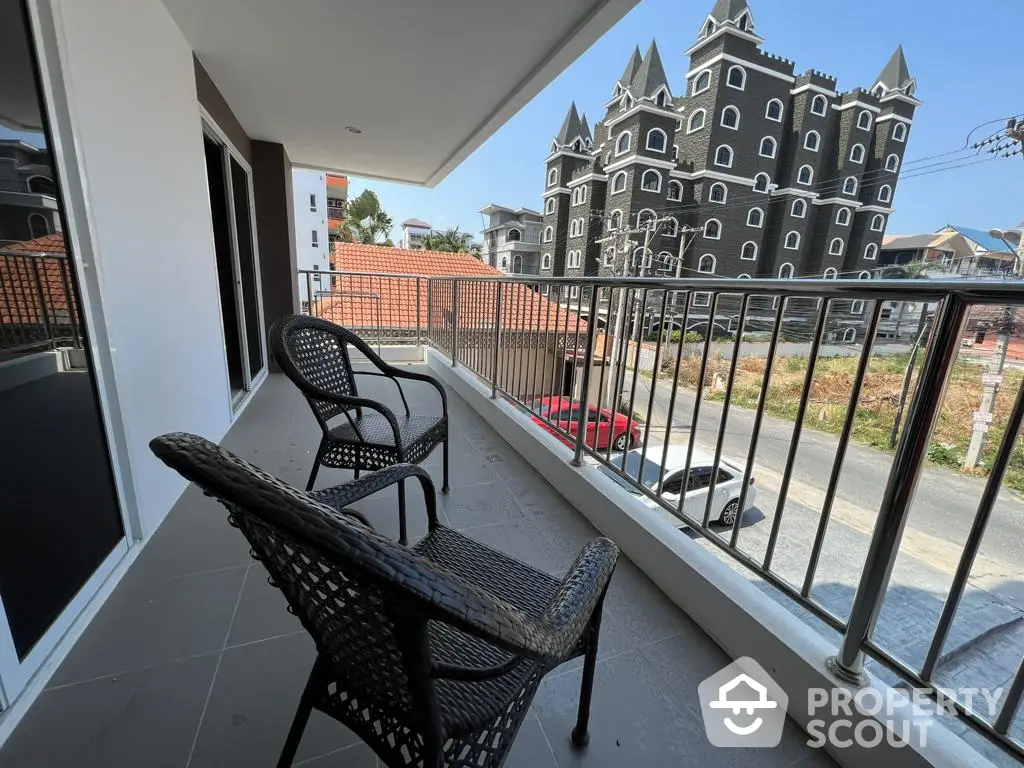 Spacious balcony with wicker chairs overlooking a unique castle-like building, offering a serene urban retreat in a distinctive neighborhood.