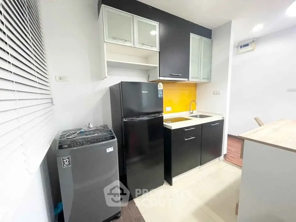 Modern kitchen with sleek black cabinets, fridge, and washing machine in compact layout.