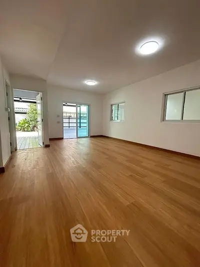 Spacious empty room with wooden flooring and large windows for natural light.