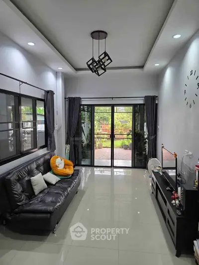 Modern living room with sleek black sofa and large glass doors opening to a garden view.