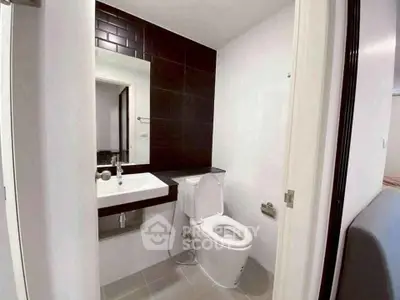 Modern bathroom with sleek design featuring a white toilet and sink against dark tiled wall.