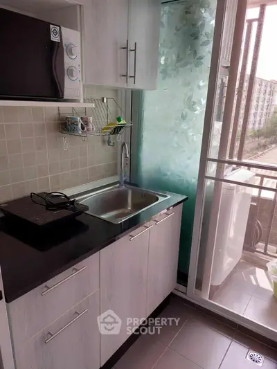 Compact kitchen with modern appliances and balcony view, ideal for urban living.