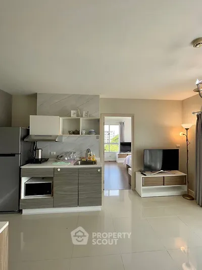 Modern open-layout kitchen with sleek appliances and cozy living area, leading to a bright bedroom.